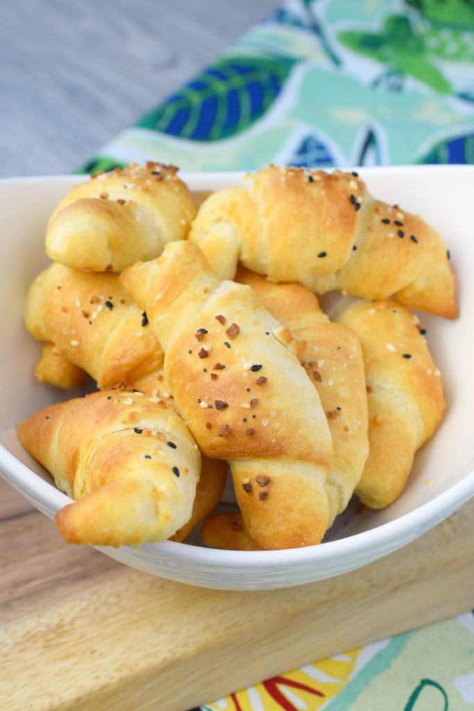 air fryer everything bagel crescent rolls in white bowl on wood plank next to floral cloth